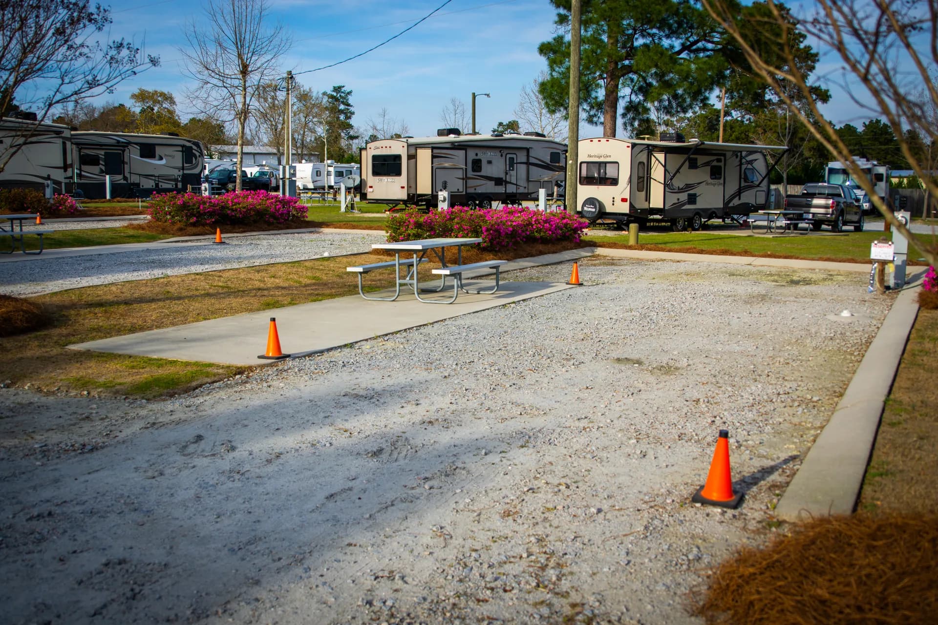 A clean, level RV site at Heritage RV Park with a concrete pad, picnic table, and azaleas in bloom